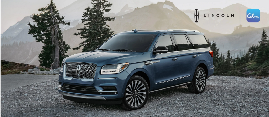 A blue Lincoln SUV parked in a scenic mountain setting with trees, featuring Lincoln and Calm logos.