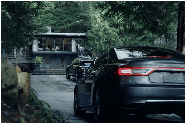 Car approaching a modern house surrounded by trees, suggesting a serene forest setting.