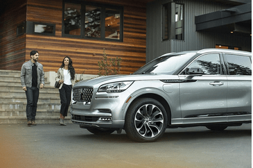 A silver SUV parked in front of a modern wooden house with a man and woman walking nearby.