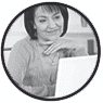 Woman smiling while using a laptop, wearing a light sweater in a home setting.