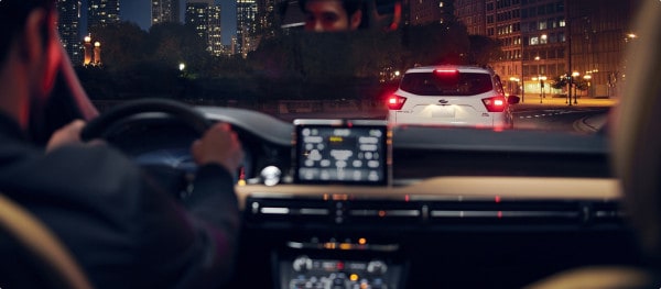 Driver's view at night with dashboard display, following a white SUV on a city street.