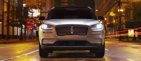 A sleek silver SUV with illuminated headlights on an urban night street.