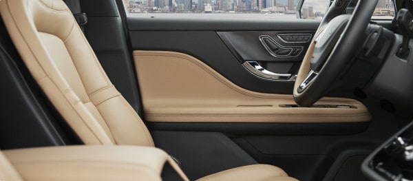 Luxury car interior with beige leather seats and a sleek dashboard, city view outside.