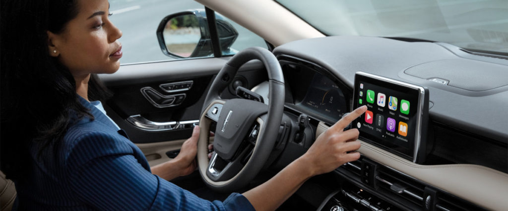 Person in a car using touchscreen navigation system on dashboard, focusing on apps.
