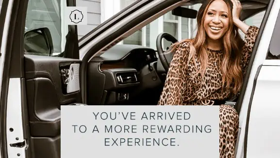 Smiling woman in leopard print outfit seated in a car, with text: "You've arrived to a more rewarding experience."