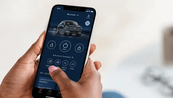 Person using a smartphone to access a vehicle app interface, displaying car controls like start and lock.
