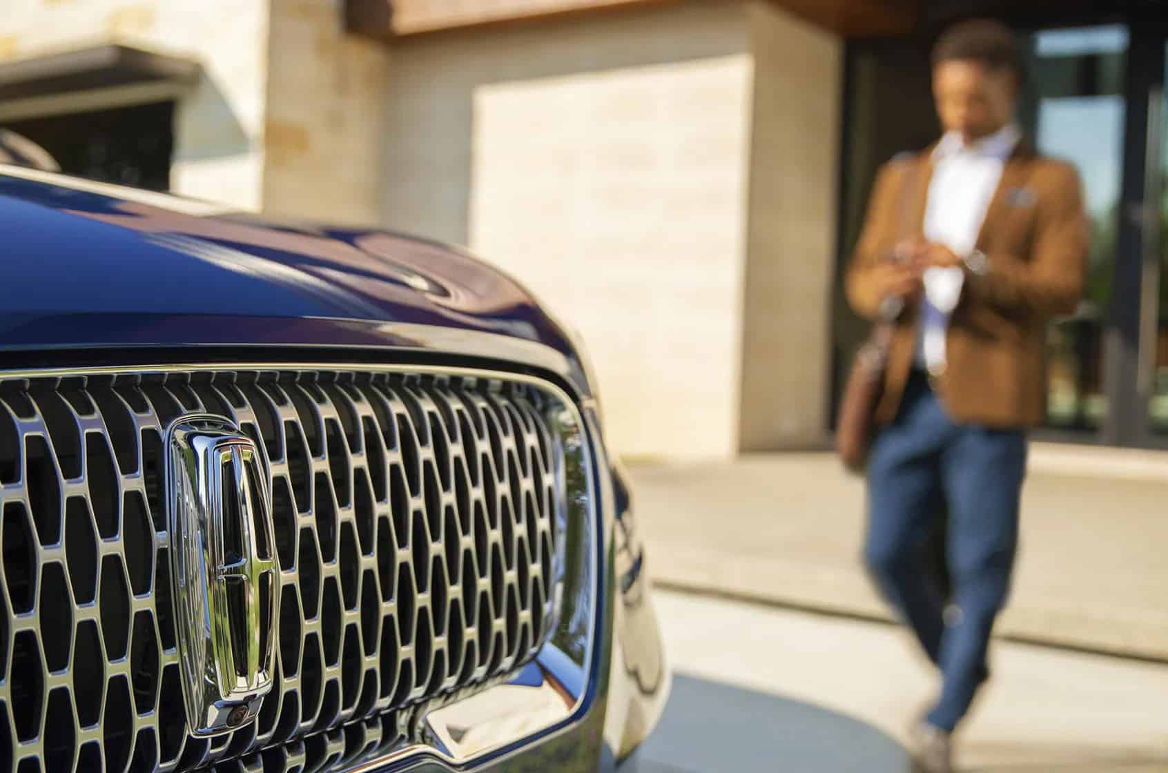 Close-up of a car grille with a person in the background, blurred, checking a phone.