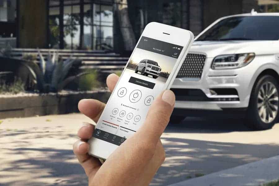 Person holding a smartphone displaying a car app interface, with a white SUV in the background.