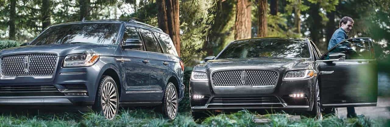 Two luxury cars parked in a forest setting, with a man exiting one vehicle. Elegant and sophisticated ambiance.