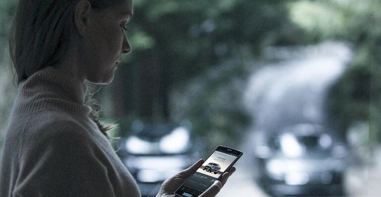 A woman using a smartphone app with cars and a scenic road blurred in the background.