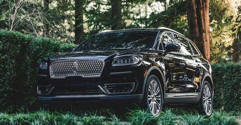 Black luxury SUV parked in a lush green forest setting, showcasing its elegant grille design.