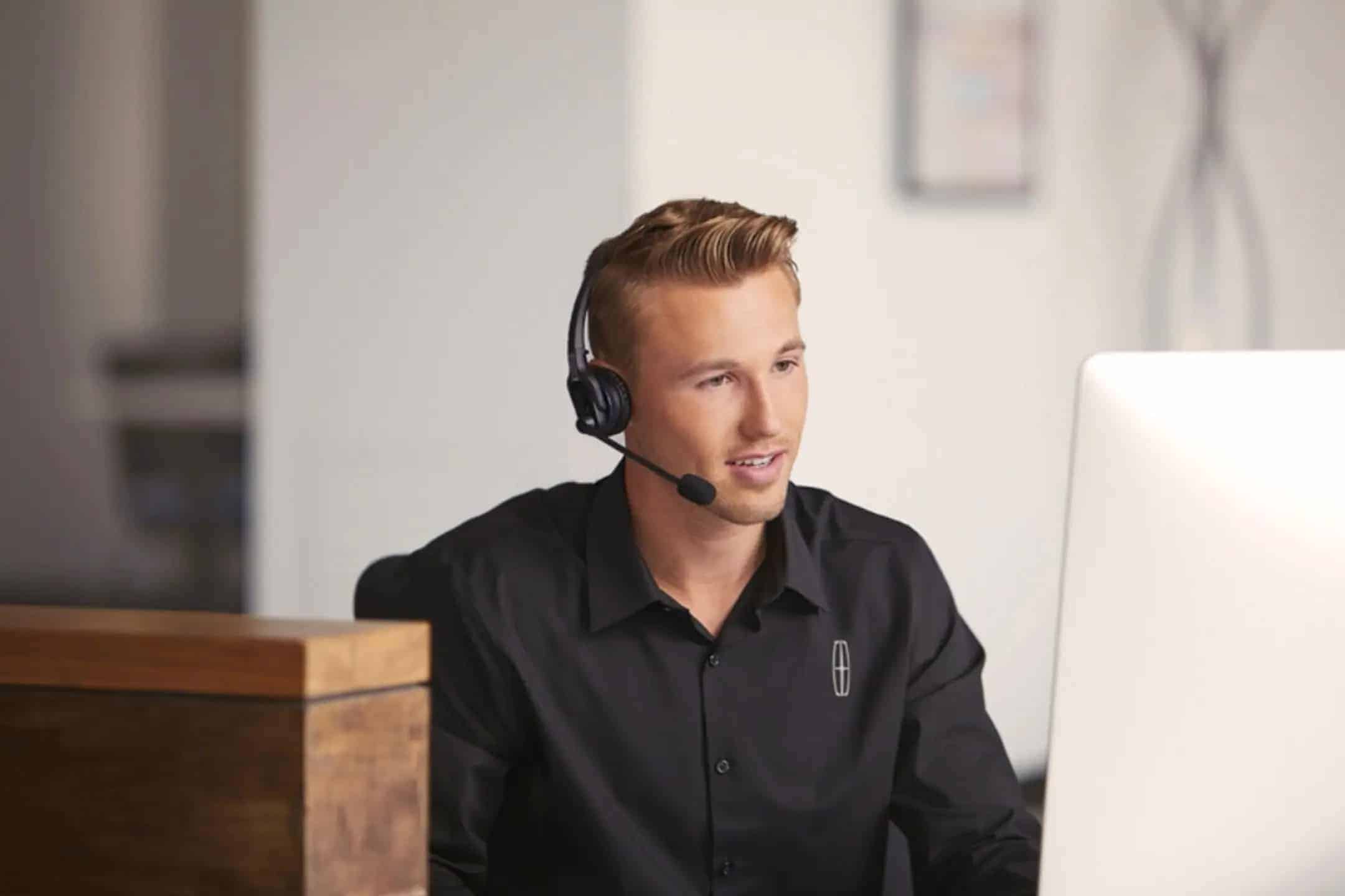 A customer service representative wearing a headset, talking while using a computer.