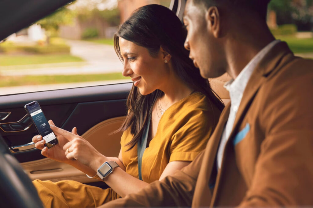 Woman using smartphone app in car, man beside her. Modern tech interaction, focused on screen.