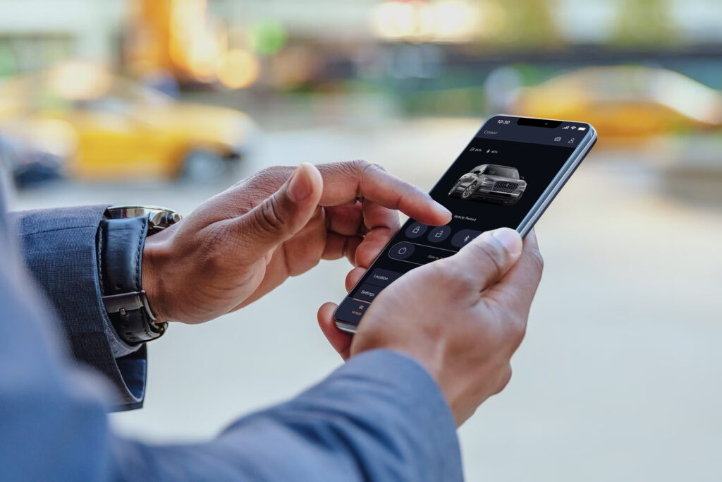 Person using a smartphone app to control car features, with yellow taxis blurred in the background.