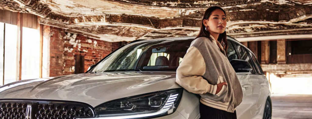 Woman leaning on a shiny white car in a vintage-style building.