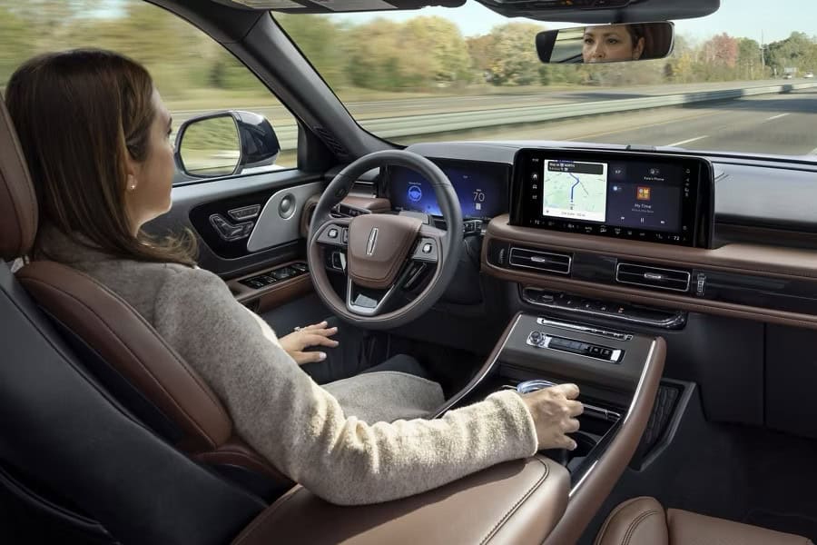 A woman enjoys hands-free driving in a modern car with an advanced navigation display on the dashboard.