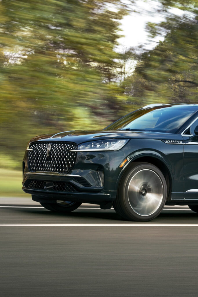 Black Lincoln Aviator SUV driving on a road with blurred green trees in the background.