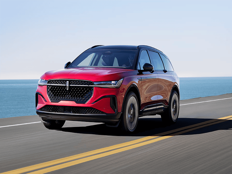 Red SUV driving on a coastal highway with ocean background under a clear sky.