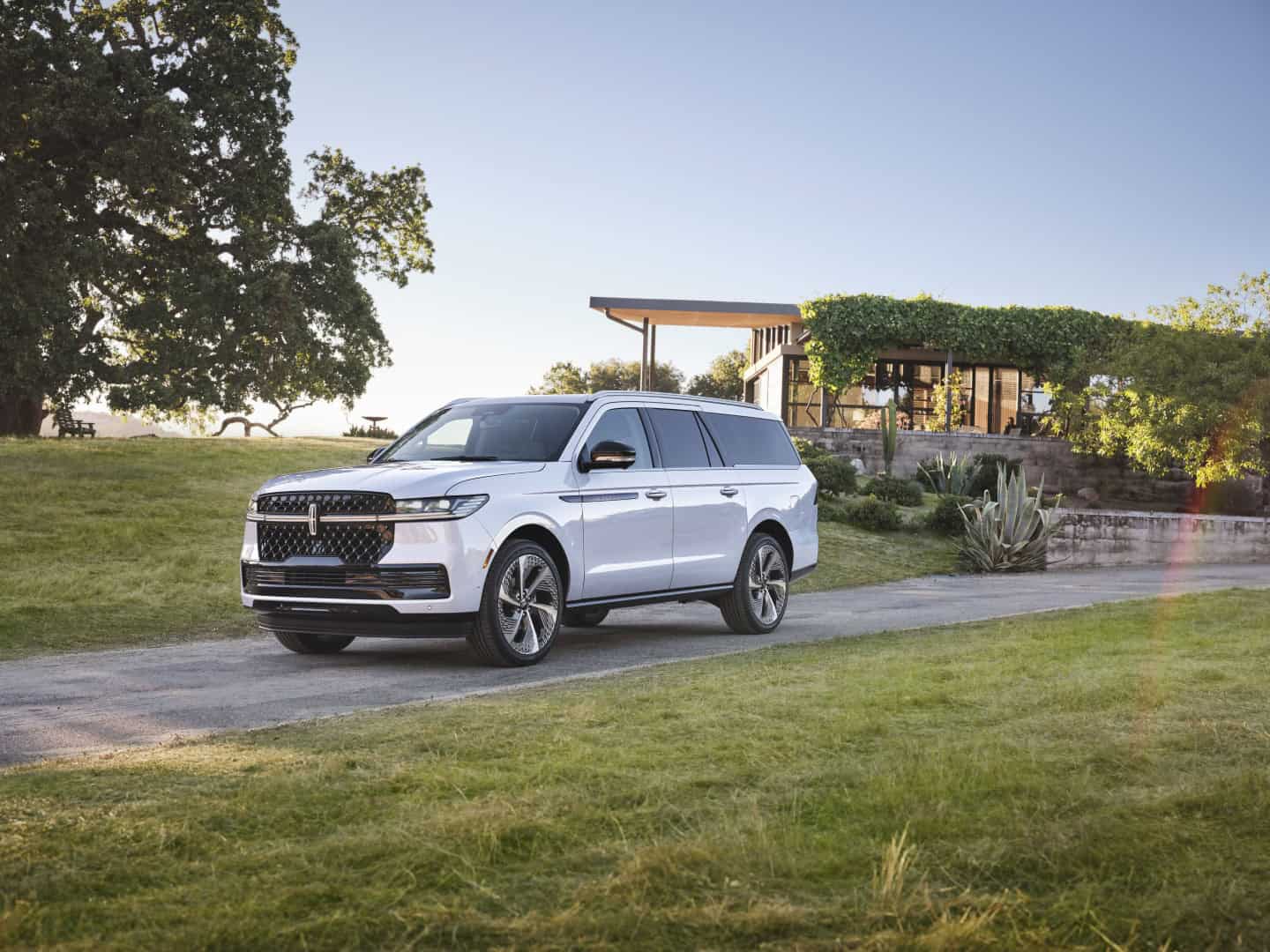 White SUV parked on a scenic driveway with a modern house and lush greenery in the background.