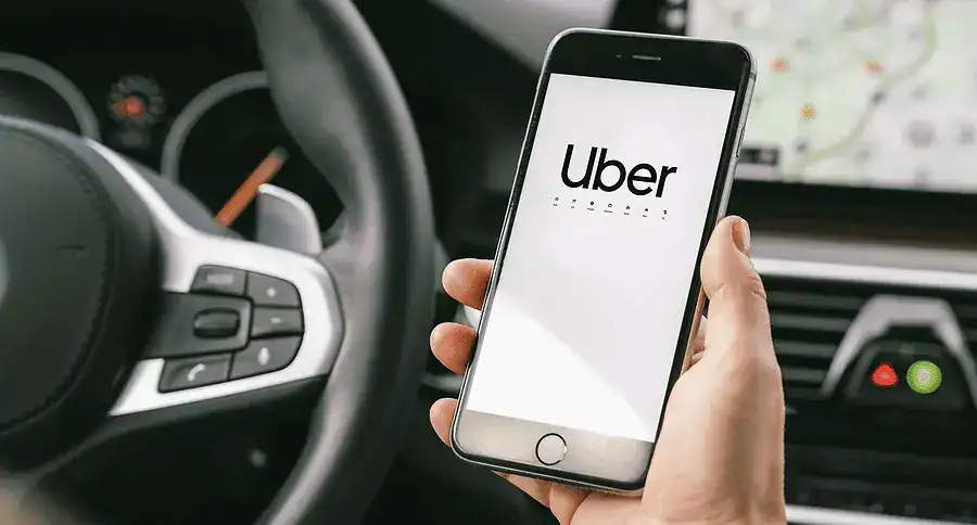 Person holding a smartphone with the Uber app open inside a car, visible steering wheel and dashboard.