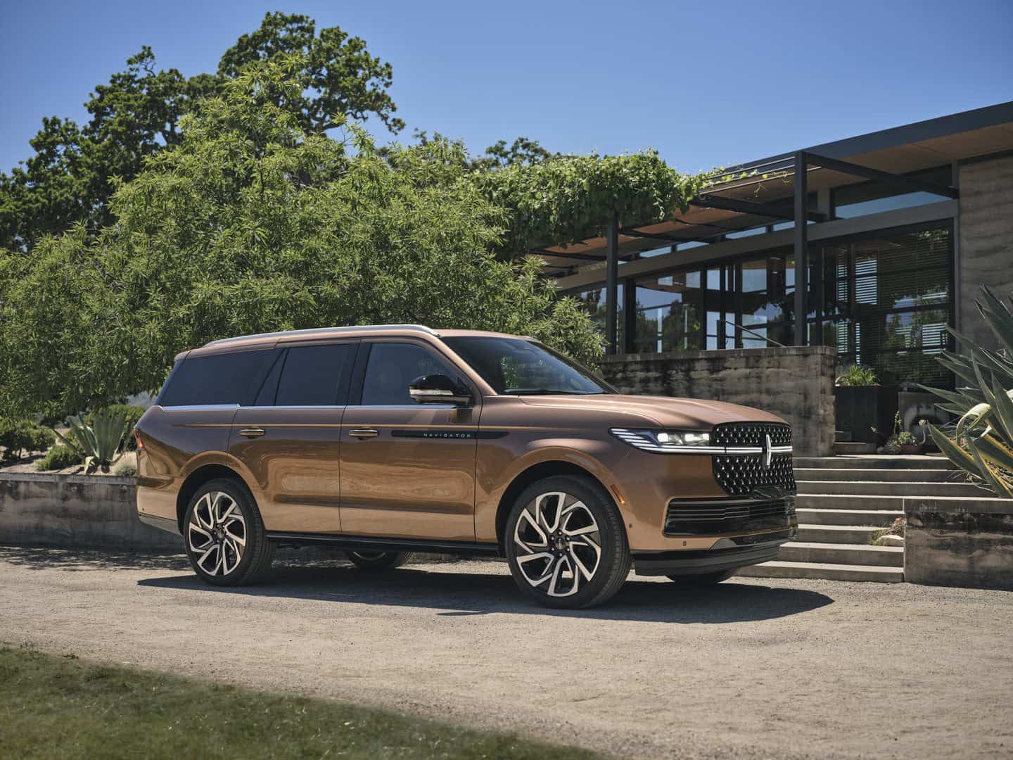 Bronze SUV parked outside a modern house with greenery, showcasing sleek design and luxury.