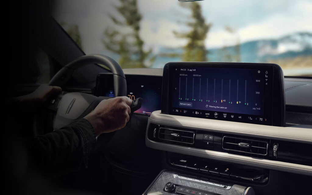 Car dashboard showing digital climate control with a person's hand on the steering wheel.